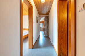 Un couloir étroit aux murs en bois et au plafond bas, qui mène à une pièce où se trouve un lit.