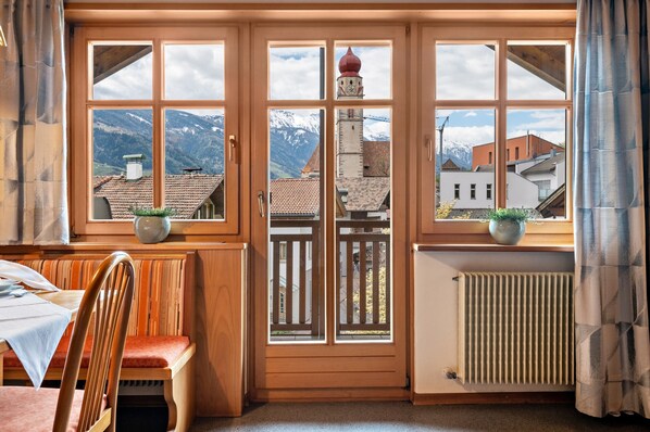 A room with a wooden bench, a table, and a view of a mountain through a window with a wooden frame.