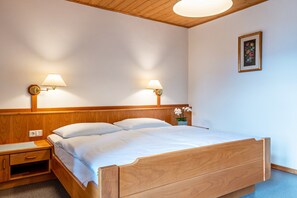 A wooden bed with two nightstands, each with a lamp, in a room with a wooden ceiling and a framed floral artwork on the wall.