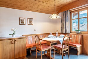 A wooden interior with a dining table, benches, and a window with a view of mountains.