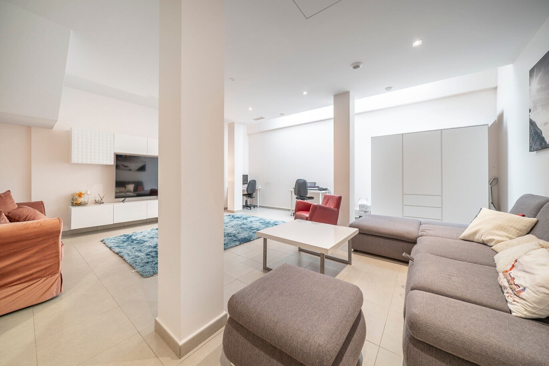 A modern living room with a sofa, ottoman, and a TV on a white cabinet.