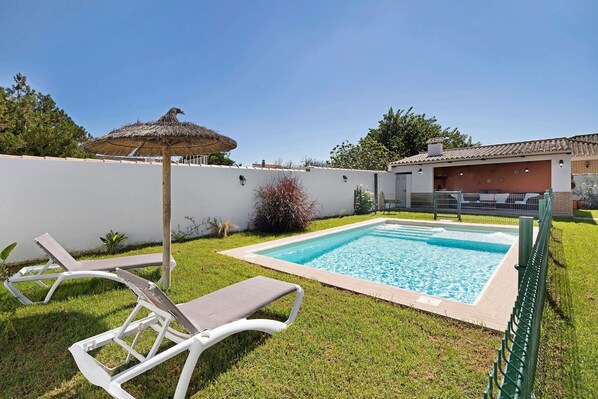 A swimming pool with lounge chairs and a thatched umbrella.