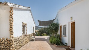 A narrow courtyard with stone walls, a tiled pathway, and a shaded area with a chair. - Finca El Porvenir with Mountain View, Pool, Whirlpool, Wi-Fi & Garden (El Gastor)