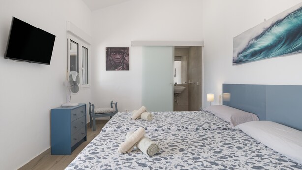 A bedroom with a bed, a dresser, a TV, a painting, and a bathroom door. - Finca El Porvenir with Mountain View, Pool, Whirlpool, Wi-Fi & Garden (El Gastor)