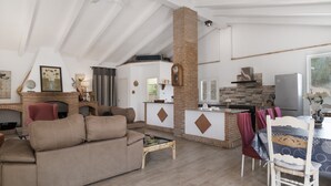 A living room with a sofa, a dining table with chairs, a fireplace, and a kitchen area with a refrigerator and stove. - Finca El Porvenir with Mountain View, Pool, Whirlpool, Wi-Fi & Garden (El Gastor)