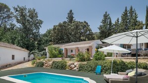 A swimming pool with a surrounding lawn, a wicker sofa, and a white umbrella. - Finca El Porvenir with Mountain View, Pool, Whirlpool, Wi-Fi & Garden (El Gastor)