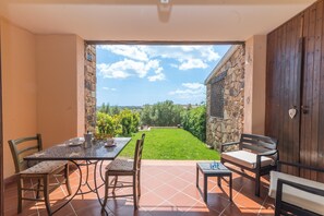 A patio with a table and chairs, a stone wall, and a view of a green lawn.
