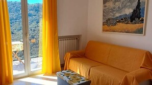 Ein Zimmer mit einer Couch, einer Bank, einem Gemälde und Blick durch eine Glastür.