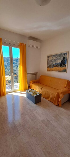 Et værelse med sofa, bænk, et maleri og udsigt gennem en glasdør.