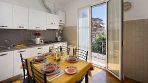 Eine moderne Küche mit weißen Schränken, einem gedeckten Esstisch und Blick auf einen Balkon mit Gebäuden.