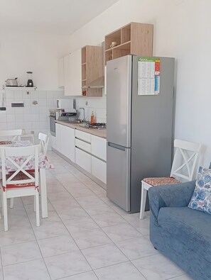 A modern kitchen with a refrigerator, wooden cabinets, a dining table with chairs, and a blue sofa. - Pet-Friendly 'Holiday Home Santa Teresa Di Riva' with Sea View (santa teresa di riva)