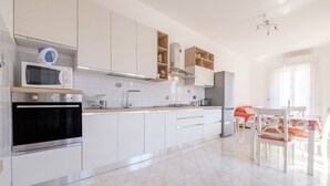 A modern kitchen with white cabinets, a built-in oven, microwave, and a dining area with a table and chairs. - Pet-Friendly 'Holiday Home Santa Teresa Di Riva' with Sea View (santa teresa di riva)