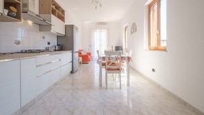A modern kitchen with white cabinets, a dining area with a table and chairs, and a window with a clock on the wall. - Pet-Friendly 'Holiday Home Santa Teresa Di Riva' with Sea View (santa teresa di riva)