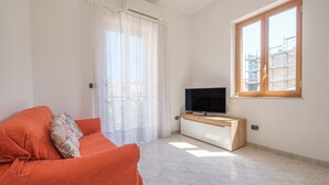 A living room with a sofa, a TV on a wooden stand, a window with a view of buildings, and a curtain. - Pet-Friendly 'Holiday Home Santa Teresa Di Riva' with Sea View (santa teresa di riva)