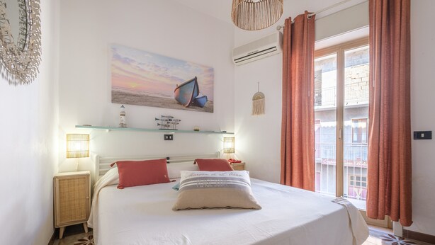 A bedroom with a bed, a wall-mounted shelf, a window with curtains, and a painting of boats. - Holiday Home 'La Marchese' close to the Beach with Terrace & Wi-Fi (Oliveri)
