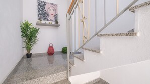 A staircase with a white handrail and granite steps, a potted plant, a small red bag, and a shelf with decorative items. - Holiday Home 'La Marchese' close to the Beach with Terrace & Wi-Fi (Oliveri)