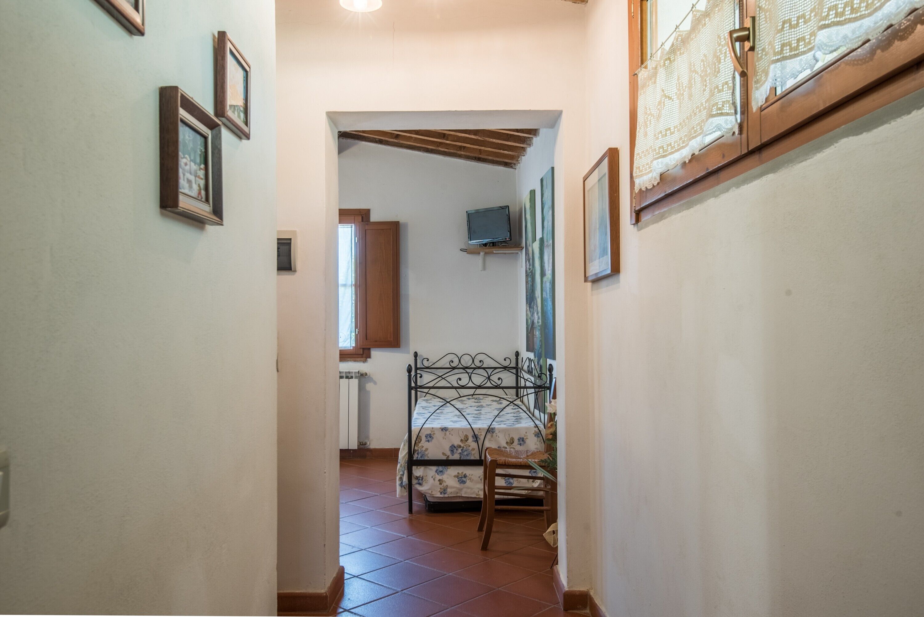Un pasillo estrecho que conduce a un dormitorio con una cama, una silla y un televisor sobre una estantería.