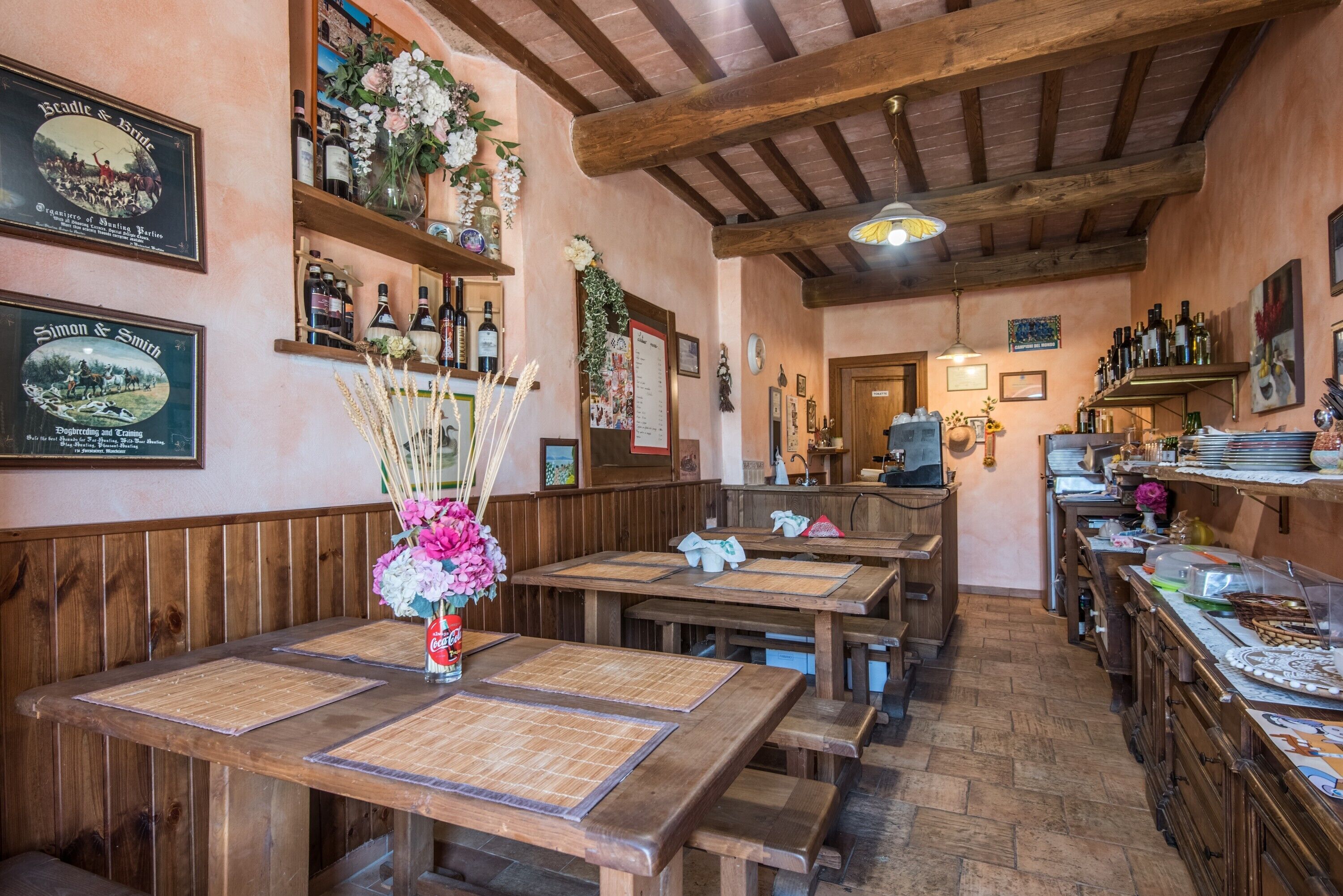 A rustic restaurant interior with wooden tables, benches, and a variety of bottles on shelves.