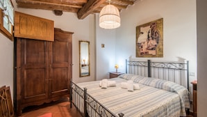 A bedroom with a bed, wooden wardrobe, a mirror, a chandelier, and a painting on the wall. - Apartment "Trilocale Etrusco" with Shared Pool, Garden & Wi-Fi (Castiglion Fibocchi)