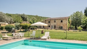 A swimming pool with lounge chairs and an umbrella, surrounded by a grassy area and a stone building. - Apartment "Trilocale Etrusco" with Shared Pool, Garden & Wi-Fi (Castiglion Fibocchi)
