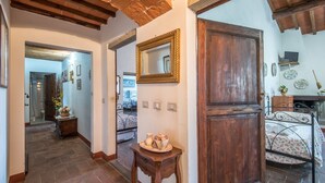 Un couloir avec une porte en bois, un miroir, une table de chevet avec un plateau, et un lit recouvert d’une couvre-lit à motifs floraux.