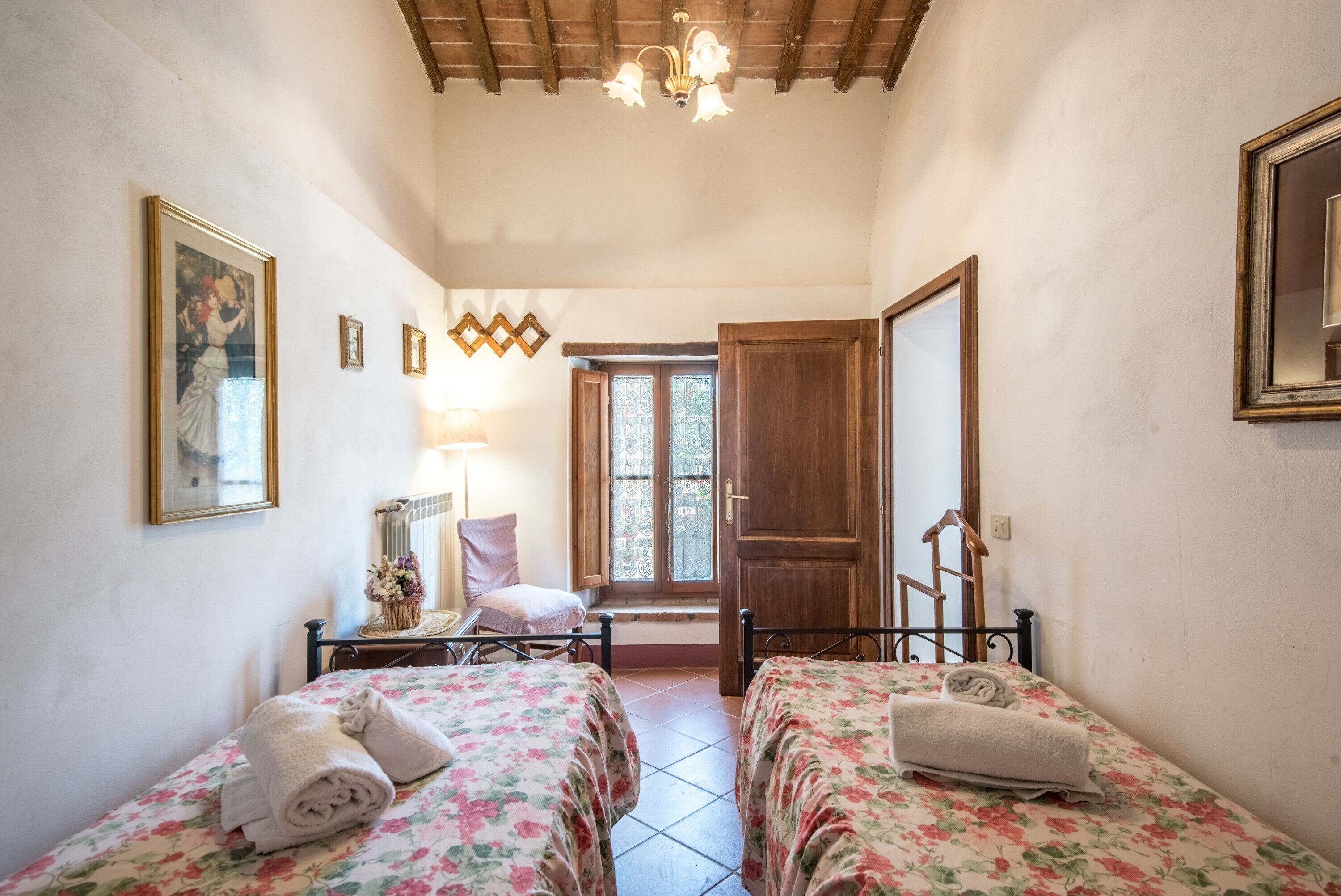 A room with two beds, a wooden door, a window, and a chandelier.