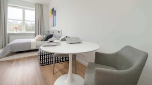 Een moderne slaapkamer met een bed, een rond witte tafel, een laptop en een grijze fauteuil.
