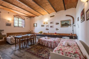 Una habitación rústica con techo de madera, una mesa de comedor con sillas, un sofá y una cama con ropa de cama estampada.