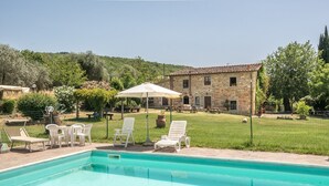Una piscina con sillas de descanso y una sombrilla, rodeada de césped y un edificio de piedra.