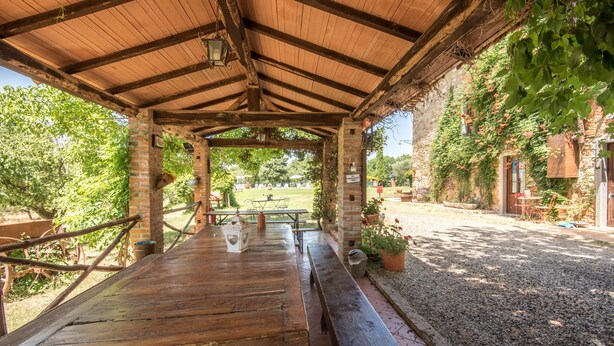Un pabellón de madera al aire libre con un muro de ladrillo, una mesa de picnic y plantas en macetas.