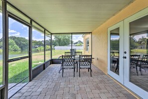 A covered patio with a brick floor, outdoor furniture, and large windows offering a view of a lake and greenery. - Lanai & Pond at Tranquil Bradenton Retreat! (Bradenton)