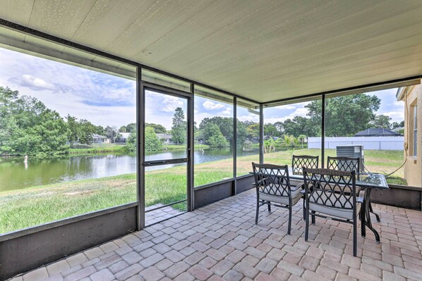 A covered patio with a view of a lake, outdoor furniture, and a brick floor. - Lanai & Pond at Tranquil Bradenton Retreat! (Bradenton)