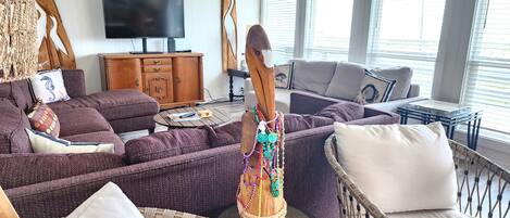 A modern living room with a large flat-screen TV, wicker furniture, and a decorative wooden sculpture.