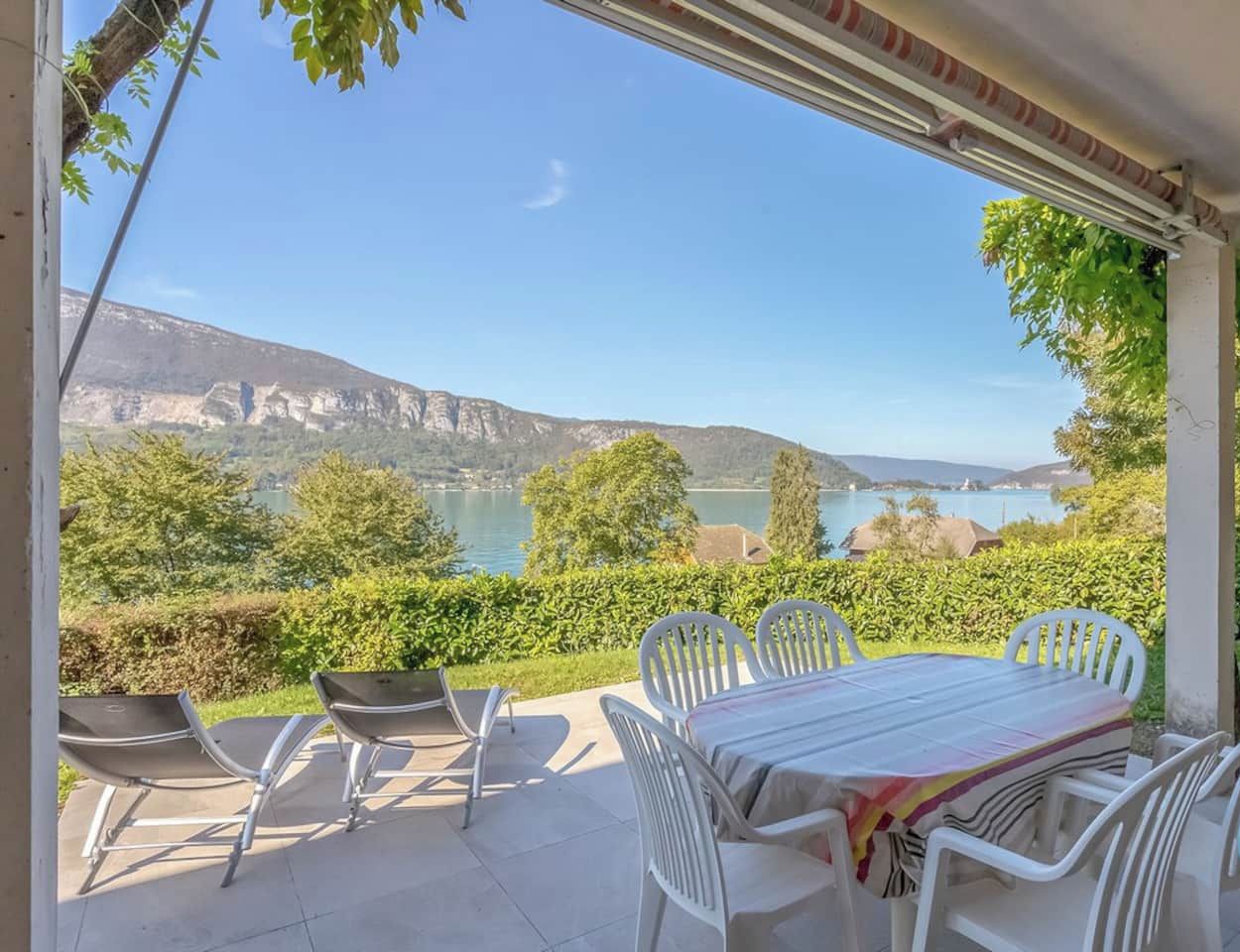 A patio with a table and chairs, overlooking a lake and mountains.