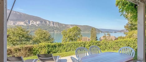 Une terrasse avec une table et des chaises, offrant une vue sur un lac et des montagnes.