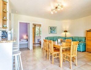 A cozy living room with a wooden dining table, teal sofa, and a wooden cabinet. - T3 Apartment – Résidence Bellevue (Talloires-Montmin)
