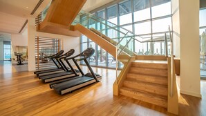 A modern gym with treadmills, wooden floors, and a glass staircase. - Bluewaters Residences Building 5 Dubai (Dubai)