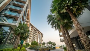 A modern building with multiple floors, large windows, and a central courtyard with palm trees and greenery. - Bluewaters Residences Building 5 Dubai (Dubai)