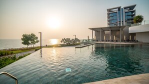 A swimming pool with a view of the sunset over the water, a modern building with balconies, and a clear sky. - Bluewaters Residences Building 5 Dubai (Dubai)