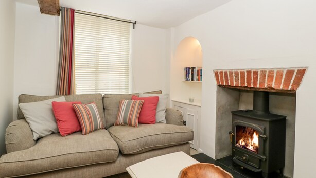A cozy living room with a sofa, a wooden bowl on a table, and a wood-burning stove. - 7 Church Lane (Lymington)