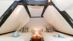 A cozy attic bedroom with two beds, a nightstand, and a lamp. - 7 Church Lane (Lymington)