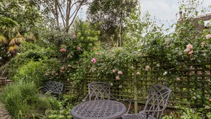 A garden with a round metal table and four chairs, surrounded by lush greenery and flowering plants. - 7 Church Lane (Lymington)