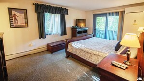 Habitación de hotel con una cama grande, un televisor sobre un mueble de madera, un banco y un balcón con vistas.