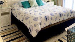 A bedroom with a bed, nightstands, a ceiling fan, a painting, a mirror, and a window with curtains. - Cozy, comfortable 2 bedroom bayside condo with WiFi, an outdoor pool, and a breathtaking view of the bay located midtown and just a few blocks from the beach! (Ocean City)