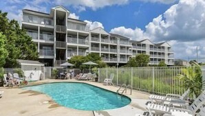 A multi-story hotel with a swimming pool, outdoor seating, and a fenced area. - Cozy, comfortable 2 bedroom bayside condo with WiFi, an outdoor pool, and a breathtaking view of the bay located midtown and just a few blocks from the beach! (Ocean City)