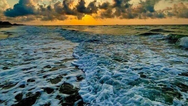 Une plage avec des vagues et un coucher de soleil.
