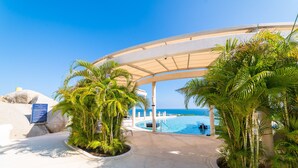 Ein Poolbereich eines Resorts mit überdachtem Gang, Palmen und freiem Blick auf den Ozean.