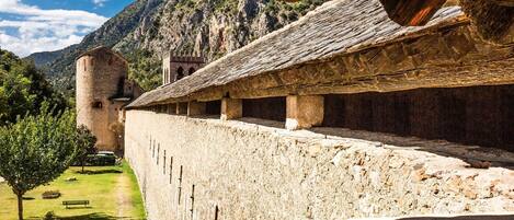 A stone wall with a thatched roof structure, a stone tower, and a bench in a mountainous landscape.