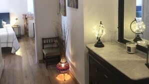 A hotel room with a wooden floor, a bed with a white and blue checkered bedspread, a bedside table with a lamp, a dresser with a mirror, and two wall-mounted paintings. - Agréable Maison en Pierre Avec Terrasse, au Coeur de la Citadelle (Villefranche-de-Conflent)