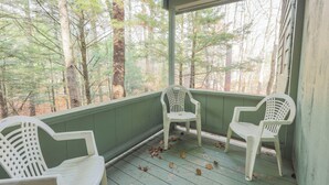 A porch with two white plastic chairs and a green railing, overlooking a forested area.